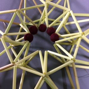Fäst yllebollar till en ring i mitten av stjärnan. vassrör formade till en stjärna med yllebollar i mitten.