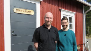 Panu Ollikkala och Jonas Sundström utanför syrsfabriken. Två män ler utanför en röd byggnad.
