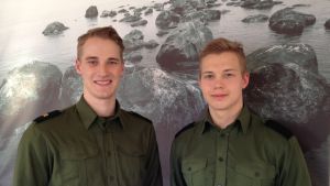 Olli Puumalainen och Janne Kinnunen från Beväringskommittéen Olli Puumalainen och Janne Kinnunen, två medlemmar i beväringskommittén vid Nylands brigad poserar framför en tavla, ett stort fotografi som föreställer hav och stenar vid strand
