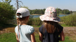 Ett stenkast från havet njuter barnen på Tallbo daghem av sommaren. Två flickor iklädda hatt och keps står och blickar ut över havet vid daghemmet Tallbo.