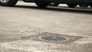 Pihakannella voi olla pysäköintialue. Kuvan sadevesikaivo ei liity Fisen kuvaamaan virheeseen. Sadevesikaivon kansi pihakannella, jossa on pysäköintialue. Taustalla autoja.