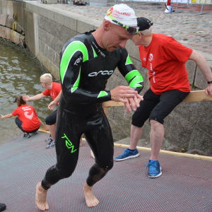 Ett triathlonlopp består av simning, cykling och löpning. man springer upp för ramp efter att ha simmat i aura å.