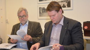 Jan Gröndahl (till höger) med dåvarande stadsdirektören Mårten Johansson år 2014. Också stadsdirektörerna har bytts ut under de åren som Norra hamnen varit aktuell. Tom Simola efterträdde Johansson och nu heter stadsdirektören Ragnar Lundqvist. Två tjänstemän i Raseborg sitter, båda i kavaj och skjorta. Den ena tittar på sina papper och den andra håller pappren i handen och tittar i kameran. Till vänster Mårten Johansson och till höger Jan Gröndahl.