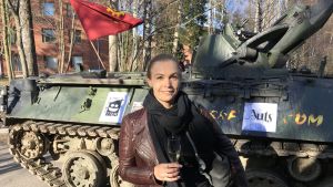 En nöjd kurator. Vendla Sandström med ett skumvinsglas framför pansarvagnen hon just anlänt i till sitt första medlemsmöte med nationen. Kurator Vendla Sandström med ett skumvinsglas framför en pansarvagn.