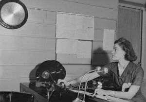 Radiokuuluttaja Birgit Lilius Fabianinkadun Radiotalossa. Aikamerkki. Kuuluttaja Birgit Lilius (myöhemmin Zilliacus) on käynnistänyt aikamerkkilaitteen ja odottaa seinällä olevan gongin kumahdusta.