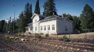Den renoverade stationsbyggnaden år 2017. Vaalea vanha puinen rautatieasema kuvattuna radan takaa, aseman takana korkeita havu- ja lehtipuita.