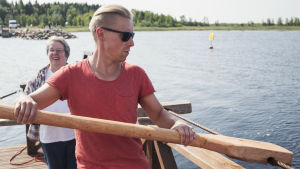 Den 300 meter långa färden tar tio minuter vid gott före. I sundet flyter en gul skylt som varnar förbipasserande båtar om färjans vajer. Toimittaja Nicke Aldén kuljettamassa kapulalossia Varjakansaaressa Oulussa, kesäilta, taustalla meri.