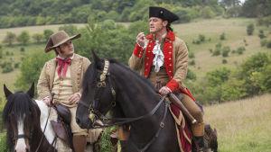 LeFou (Josh Gad) lyssnar intensivt då Gaston (Luke Evans) lägger ut texten om sin egen förträfflighet. LeFou (Josh Gad) och Gaston (Luke Evans) sitter på varsin häst och talar med varandra.