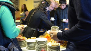 På plats var också en del av den grupp flyktingar som anlände för ett år sedan. Mänskor tar för sig av kaffe och bakverk.
