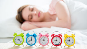 En kvinna som sover och har många väckarklockor bredvid sängen.