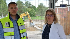 Erik Rönnqvist och Ulrica Nyström. Erik Rönnqvist till höger med arbetsväst på sig. Till höger står rektor Ulrica Nyström med vit kofta. I bakgrunden ser man ett byggstängsel och en grävskopa.