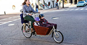 Sandra vill gärna se fler lastcyklar i stadsbilden. En kvinna cyklar men två barn sittandes fram i en korg och ett barn på pakethållaren.