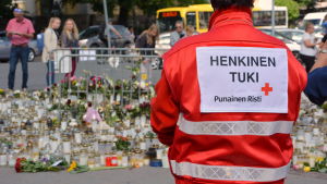Utredningen kräver bättre stöd för offren och de anhöriga i liknande olyckor och våldsdåd. Person med röda korsets väst vid gravljus på Åbo torg.