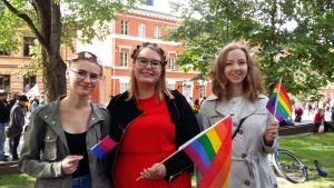 Miranda, Rebecka och Elin på Turku Pride 2017 Tre unga kvinnor med regnbågsflaggor i händerna står framför Katedralskolan i Åbo