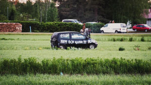 Den här gången tog det 9 minuter och 14 sekunder för bilen att börja brinna. En svart bil ute på en åker som har texter sprayade på den som t.ex. "Kom och gissa!"