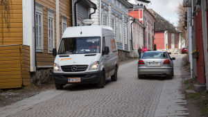När postens skåpbil stannat mitt på vägen får de andra bilarna krångla sig förbi på den smala gatan. bild på bilar som kör