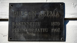 Skylten på stationsväggen informerar om att den senaste grundsaneringen gjorts år 1997. Kyltti seinässä, jossa lukee "Pulsan asema, rakennettu 1870, peruskorjattu 1997"