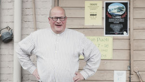 Kari Savola on Vääksyn myllyn mylläri. Mies seisoo kädet puuskassa ulko-oven edessä ja nauraa.