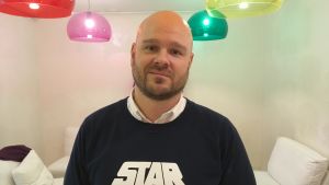 Andy Prinkkilä är projektledare på reklambyrån C2 i Vasa. Andy Prinkkilä står i ett rum där färgglada lampor hänger från taket. Han bär en tröja med en star wars logo på sig.