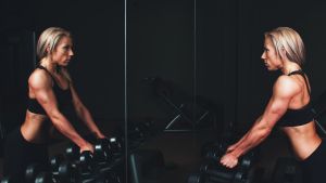 Det är populärt för både killar och tjejer att styrketräna och gå på gym. kvinna i konditionssal ser sin muskulösa kropp i spegeln