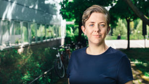 Maria Brandén forskar i sociologi vid Stockholms universitet. maria branden står under ett skuggigt träd på sommaren. hon bär en blå tröja.