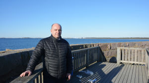 Vd Anders Ahlvik har tre hamnar på sitt bord - Västra hamnen, Koverhar hamn och Yttre hamnen. En bild på en man som står vid havet. Han lutar mot ett staket. Mannen heter Anders Ahlvik och han är vd för Hangö hamn