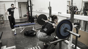 Elin Hassel tränar grenen hon tycker minst om: knäböj. En kvinna och en man i ett gym. Kvinnan gör knäböj med en stång och vikter på axlarna som väger sammanlagt 80 kg. Mannen tittar på.