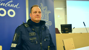 Jukka Sillanpää. överkonstapel jukka sillanpää har uniform på sig och står med en bakgrund av en polisbanderoll.