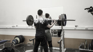 En partner kan passa dig och samtidigt hålla koll på tekniken. En kvinna och en man i ett gym. Kvinnan har en skivstång på axlarna och mannen står bakom och vaktar så hon inte tappar stången.