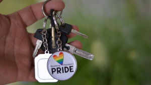 Så här ser nyckelringen ut! En hand som håller i en nyckelring. I nyckelringen hänger en rund liten bricka där det står Raseborg Pride.