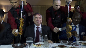 Brasiliens president Michel Temer lugnade ner och bjöd ambassadörer från länder med stor köttimport på biffrestaurang i söndags . Brasiliens president Michel Temer med servitörer som skär kött från stora spett på vardera sidan om sig.