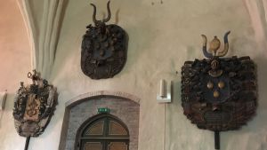 På väggen i Pojo kyrka hänger adliga begravingsvapen. Stora utsirade trävapen på en kyrkvägg.