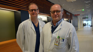 Professor i barnortopedi och överläkare Ilkka Helenius (vänster) och avdelningsöverläkare Olli Pajulo genomförde operationen med sitt team. Två manliga läkare, en ung och en i övre medelåldern, står i en sjukhuskorridor med vita läkarrockar på sig.