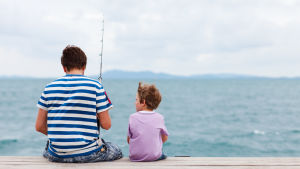 Även många pappor lever som singelföräldrar. En pappa sitter med sin son på en brygga med ett fiskespö. I bakgrunden syns hav och en molnig himmel.