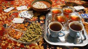 Illat iftar-aterian jälkeen ovat perheen ja ystävien yhdessäolon aikaa Kuvassa itämaisella matolla teekuppeja, pelikortit ja pähkinöitä