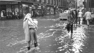 Helsingin keskustassa tulvi v. 1974 Äiti kantaa lapsen tulvivan kadun yli Helsingissä v. 1974