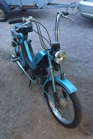 Den lilla mopeden. Med den lilla lilla sitsen. En gammal moped. Den är ljusblå och har ett högt styre och en liten sits.