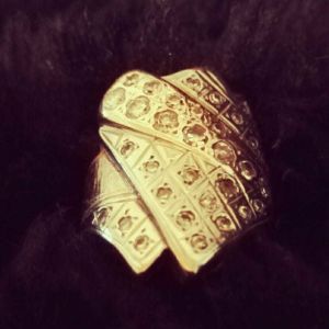 Ringen föreställer två pappersark och en fjäderpenna. En guldring som föreställer två pappersark och en fjäderpenna.