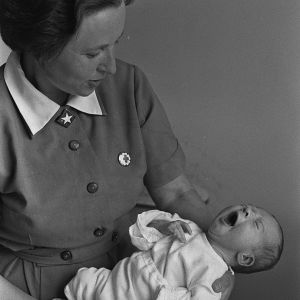 Kätilö ja vauva neuvoloiden alkuaikoina. Itkevä vauva kätilön sylissä (1960-luku).