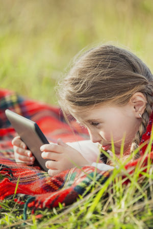 Tyttö makaa nurmikolla tablettitietokoneen kanssa.