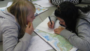 Kaksi tyttöä tekee luokan lattialla tehtäviä kartan kanssa.