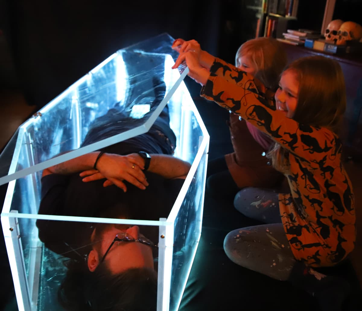 Taiteilija Ilmari Wärrin tyttäret nostavat pleksilasisen arkun kantta.