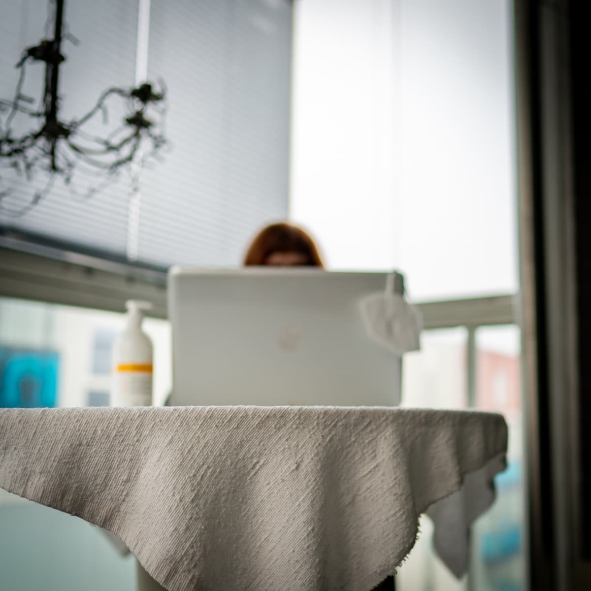 Nainen työskentelee kannettavalla tietokonella, koneen näytön kulmalla roikkuu kasvomaski.