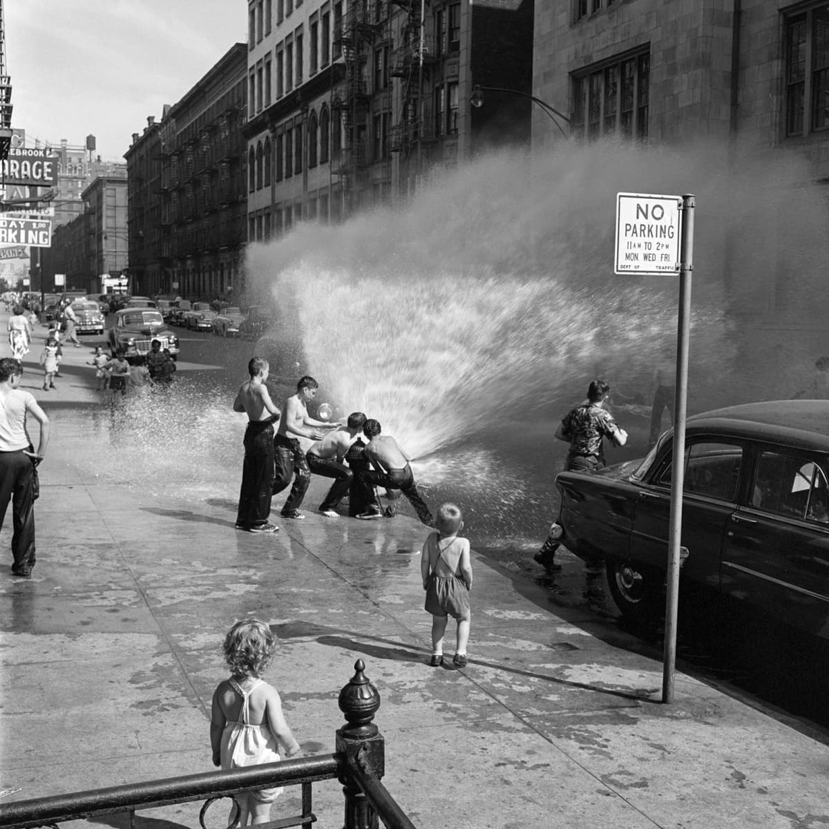 Lapset suihkuttavat vettä palopostista kadulla.