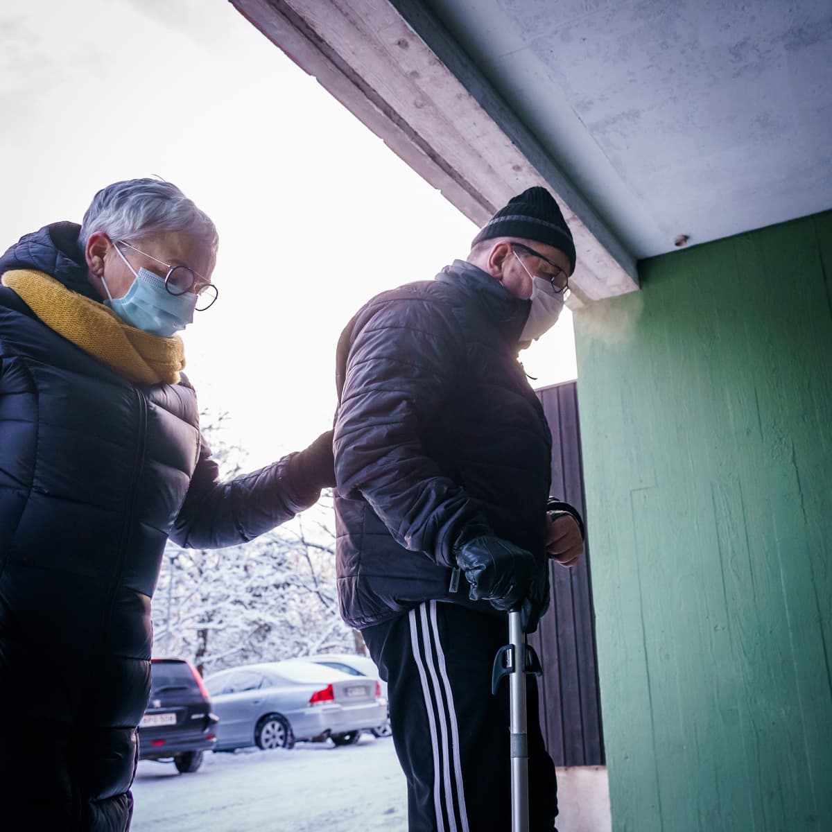 Omaishoitaja Marja-Liisa Saarinen tukee kepin kanssa kulkevaa miestään Reijoa matkalla taksista kotiovelle.