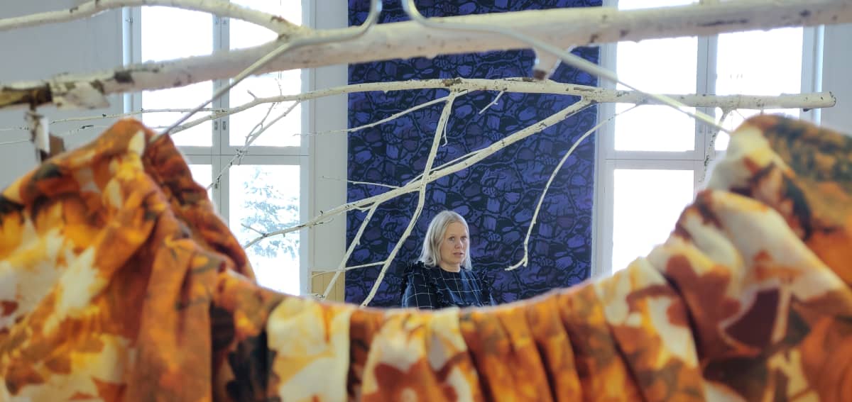 Paola Suhonen suuressa näyttelytilassa keskellä erilaisia kankaita.