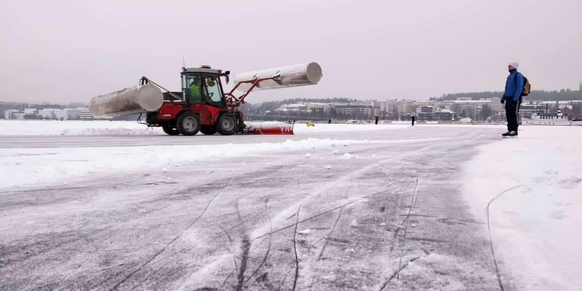 Pieni traktoriaura Jyväsjärven jäällä tekemässä retkiluistelurataa. Luistelija katsoo auraa radan sivusta.