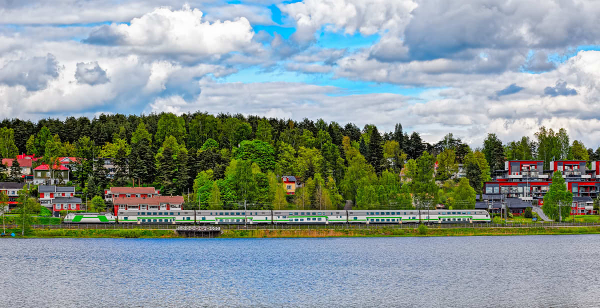 Kuva suomalaisessa maisemassa kulkevasta junasta. Metsää takana, vettä edessä. 