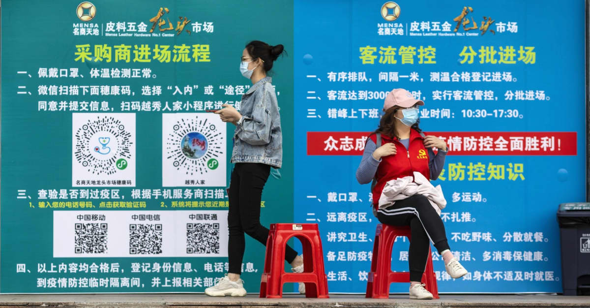 Nainen kävelee ja toinen istuu, taustalla seinän peittävä juliste.