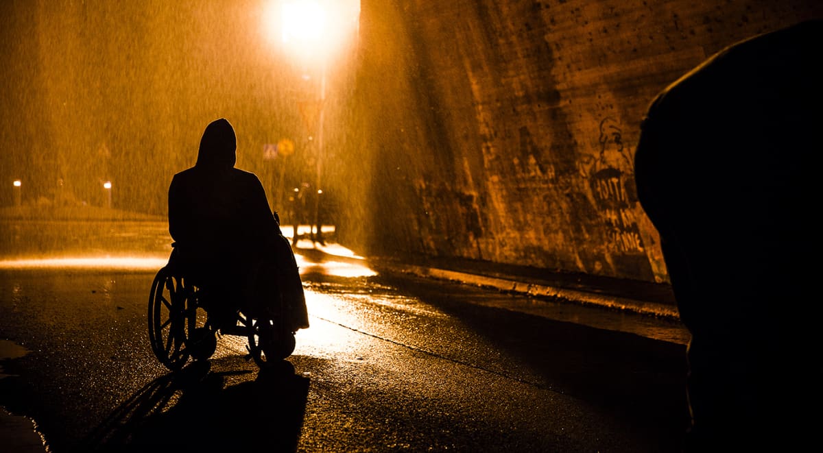 Pyörätuolissa istuvan miehen siluetti tihkusateisessa yössä, otos elokuvasta Rendel